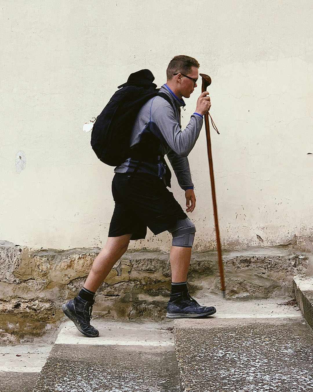 Peregrino haciendo el camino de Santiago sube unos escalones de piedra con un bastón de madera y una rodillera.
